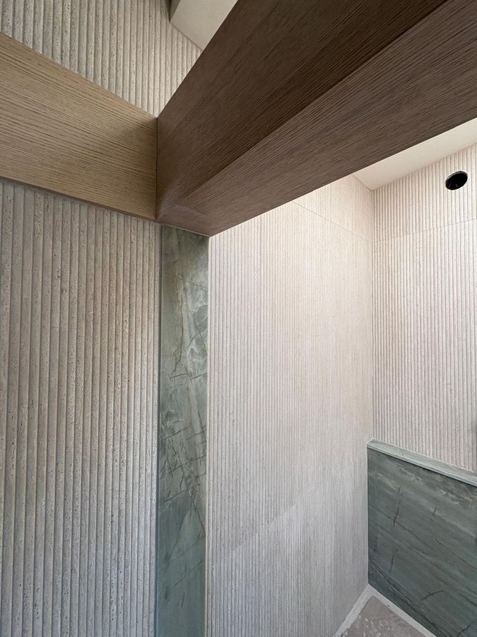 Fluted travertine-look shower walls with green marble accent and oak beam